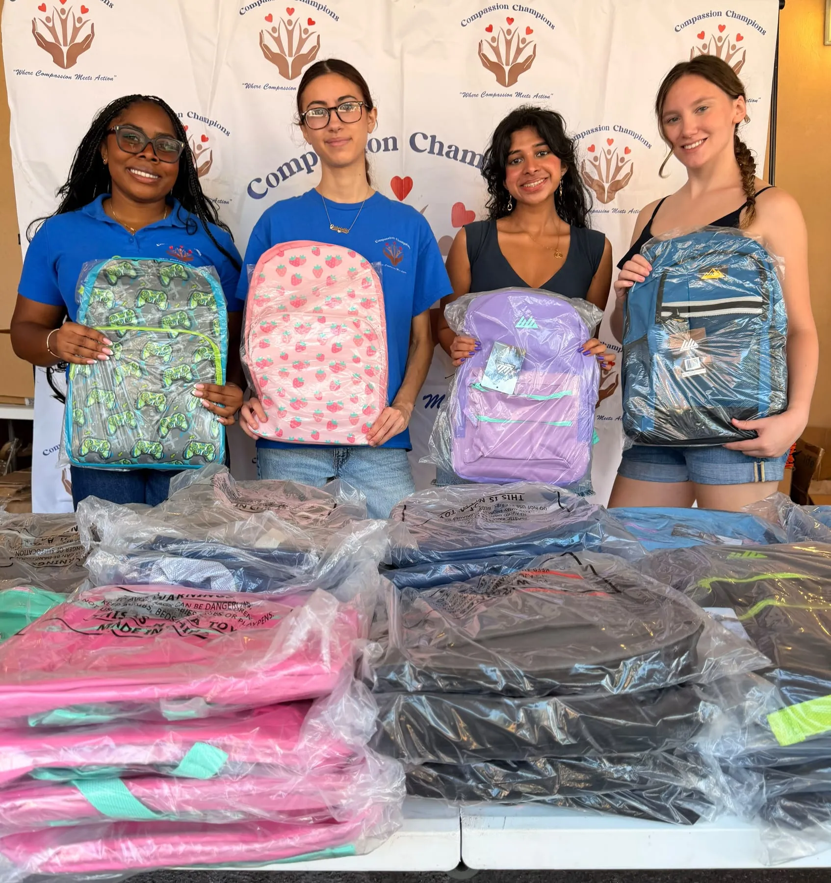 Volunteers holding up new backpacks above tables of donated bags